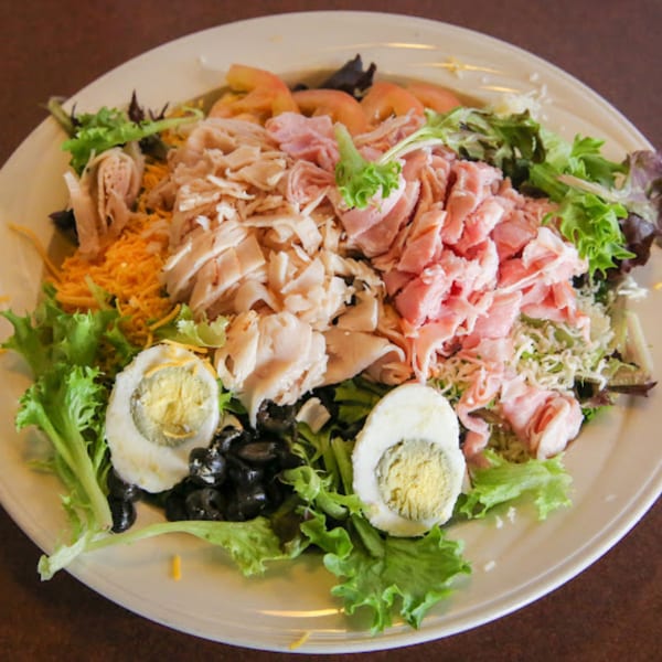 A large chef salad with ham, turkey, cheese, tomatoes, olives, and hard-boiled eggs.