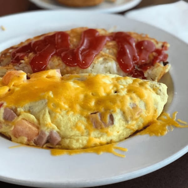 A cheesy omelet with ham and hash browns topped with ketchup on a white plate.