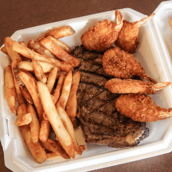 Steak and fried shrimp with a side of french fries in a white takeout container.