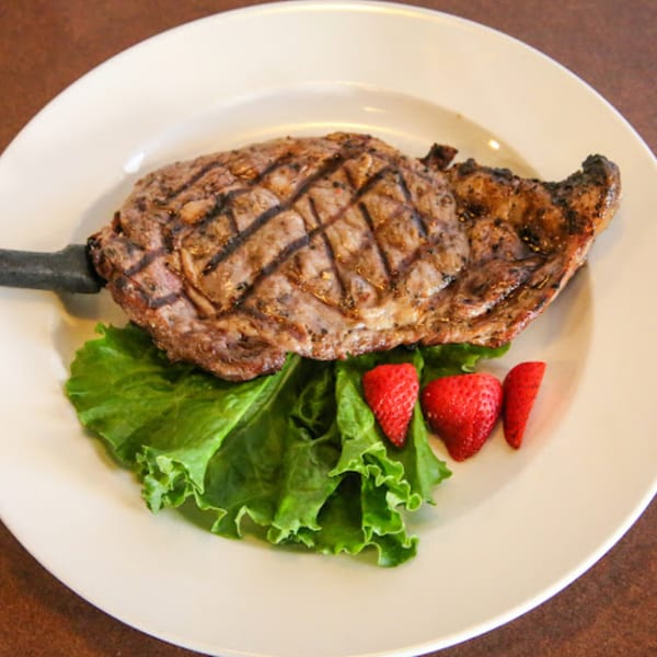 Grilled steak with grill marks, served on a bed of lettuce with sliced strawberries on a white plate.