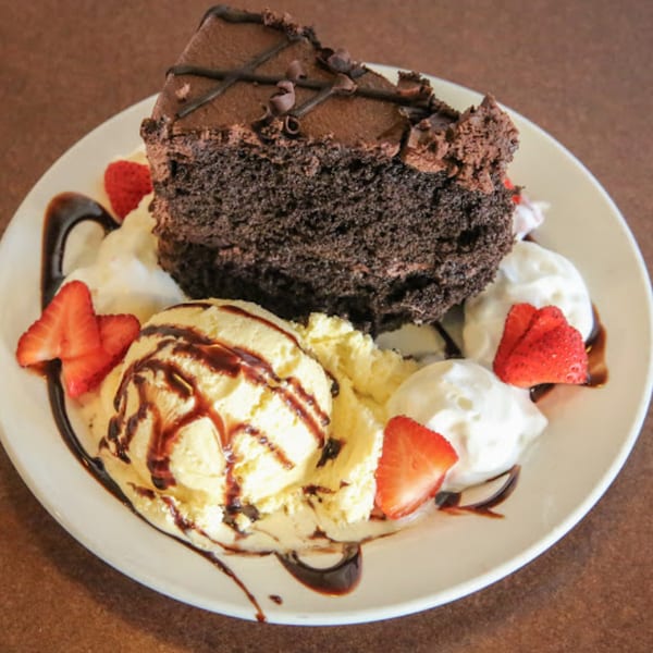 A slice of chocolate cake with vanilla ice cream, whipped cream, strawberries, and chocolate drizzle.