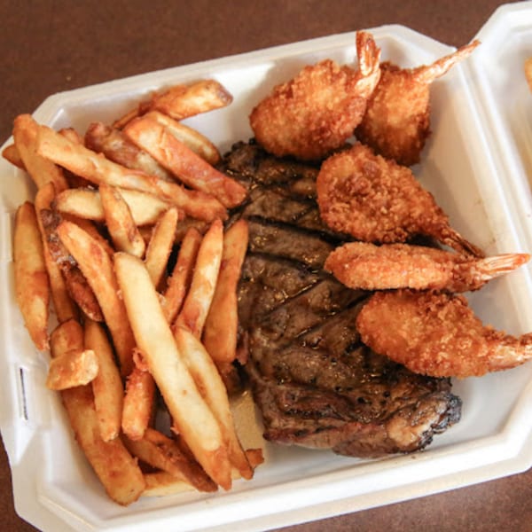 Sterling Café's steak and fried shrimp with a side of french fries in a takeout container.